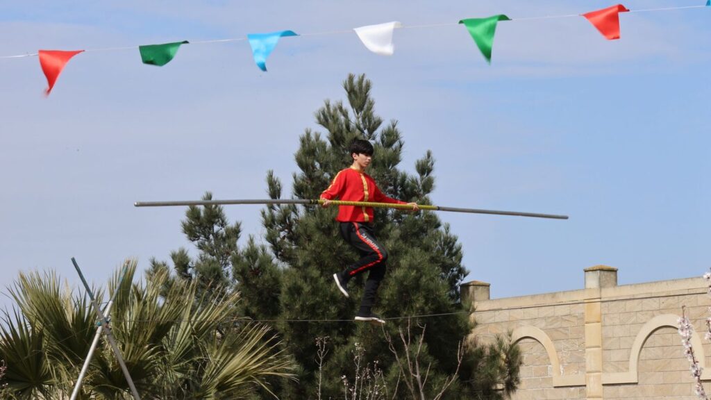 Un funambule en costume rouge avance sur un fil, balancier en main
