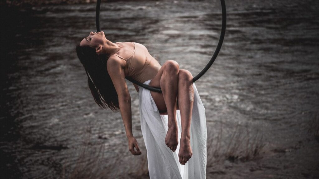 Une acrobate suspendue à un cerceau aérien, en extérieur