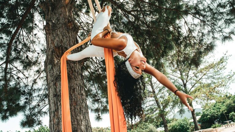 Une acrobate suspendue à des tissus aériens entre des arbres